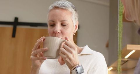 Mature woman sipping from ribbed beige mug in cozy modern kitchen