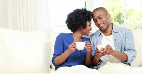 Young Couple Enjoys Cozy Moment with Warm Drinks on Couch