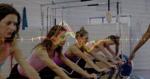Women in gym exercising on stationary bikes focusing intently