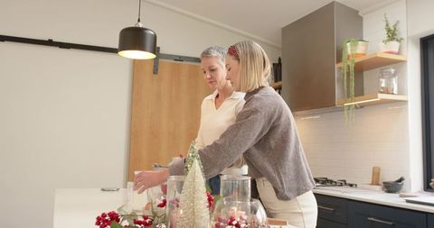 Mother and daughter arranging festive holiday decorations on modern white kitchen counter
