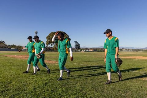 Four baseball teammates walking off field after game in green and yellow uniforms