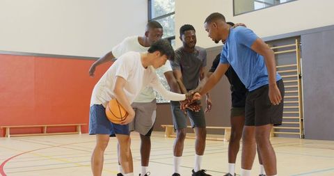 Five players huddling on indoor basketball court before game showing teamwork and focus