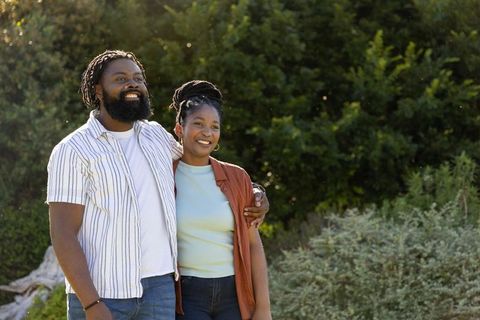 African american couple smiling and embracing outdoors on sunlit park walk, casual love