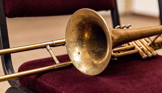 Vintage brass trombone resting on maroon velvet chair showing patina and dents close-up