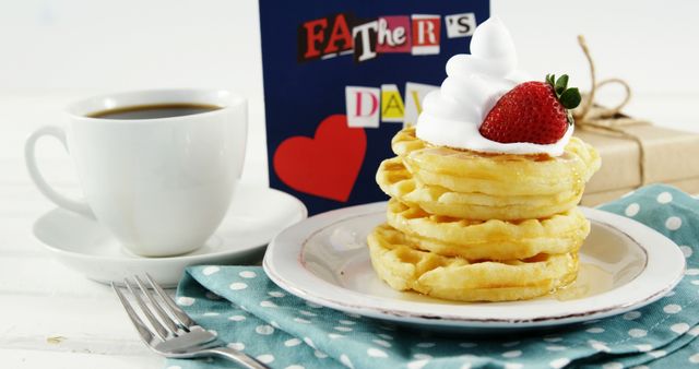 Stacked waffles topped with whipped cream and a slice of strawberry sit beside a cup of coffee and a gift wrapped in kraft paper. Father's Day card is prominently displayed. Ideal for showcasing Father's Day celebration ideas, gifting themes, and breakfast recipes.