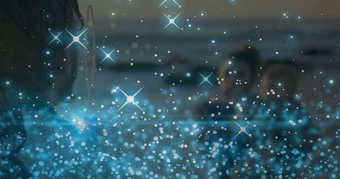 Surfer silhouette watching family at ocean dusk with dreamy blue bokeh sparkle overlay