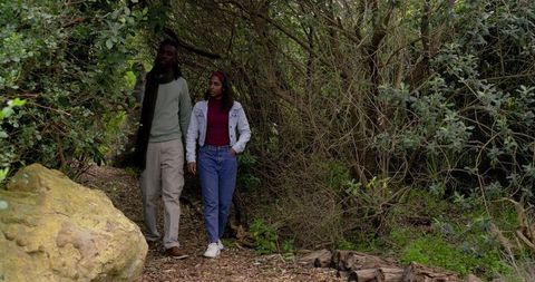 Walking Through Woodland Canopy: Diverse Couple Exploring Narrow Forest Trail