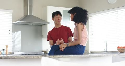 Young multicultural couple chatting on modern kitchen island with smartwatch and natural light