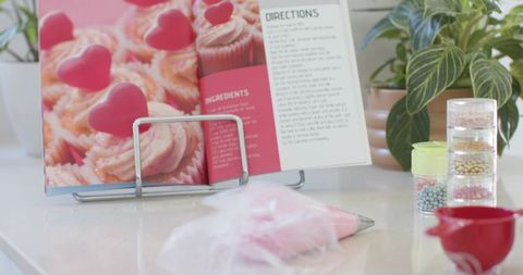 Pastel cupcake recipe book on stand with piping bag, frosting and sprinkles