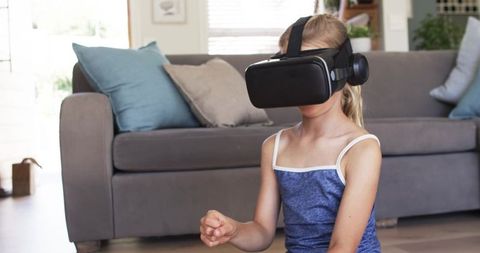 Young girl exploring virtual reality on living room floor wearing vr headset, casual top