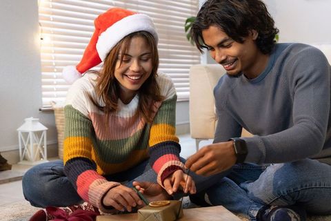 Young couple wrapping christmas gifts with twine and dried orange slice, cozy home holiday