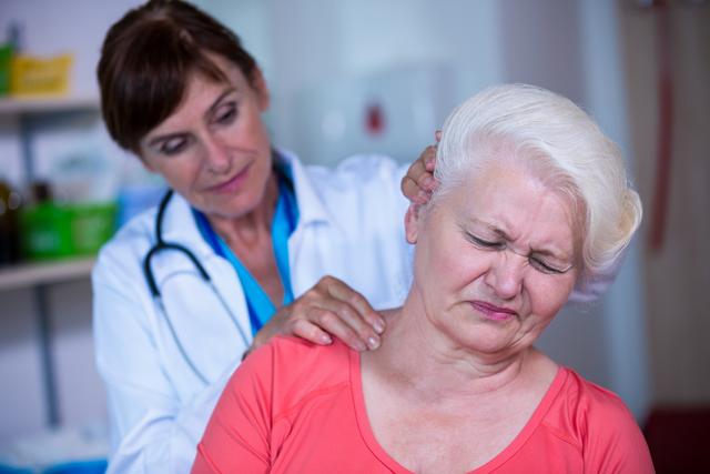 Female doctor examining elderly patient in hospital. Senior woman experiencing neck pain while receiving medical consultation. Useful for healthcare, medical services, patient care, and senior health-related content.