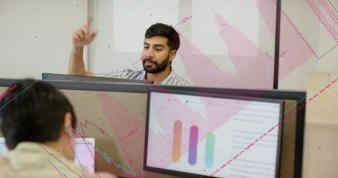 Bearded man waving and typing while laughing with coworker over dashboard monitors