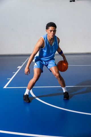 Teenage Basketball Player Dribbling on Indoor Court in Blue Uniform
