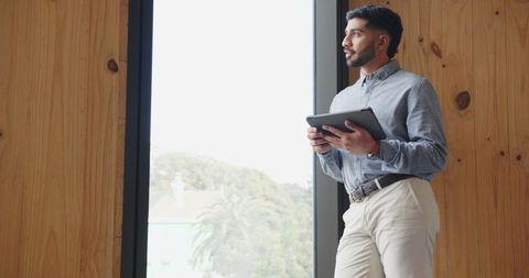 Professional Man Using Tablet by Large Window in Modern Office