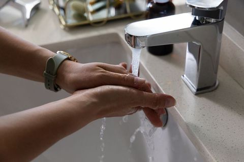 African american woman washing hands under chrome faucet in minimalist bathroom countertop