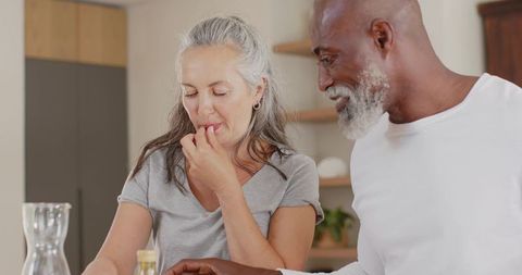 Mature couple tasting homemade dish in modern kitchen, african american man leaning in