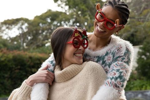 Friends embracing and smiling wearing festive glasses and cozy sweaters outdoors