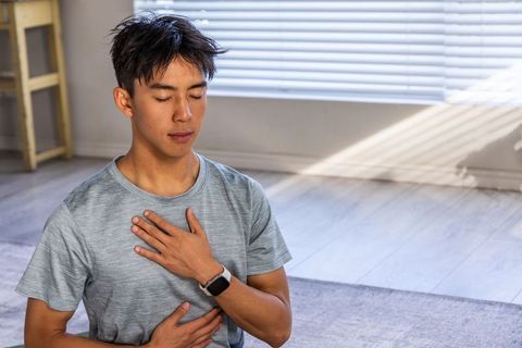 Asian man practicing mindful breathwork at home with smartwatch in sunlit minimal space