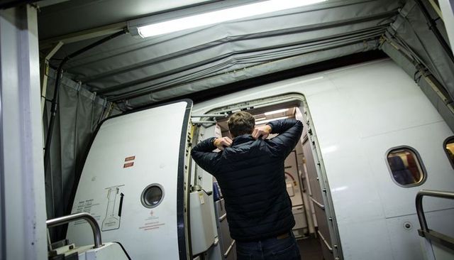 Male traveler boarding aircraft via jet bridge adjusting quilted jacket entering cabin