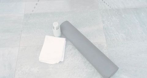 Minimalist gray yoga mat with towel and water bottle on cool tiled floor for home workout