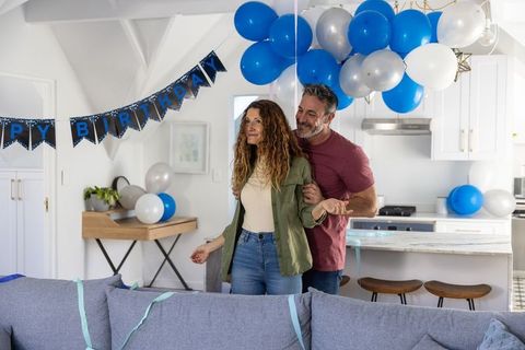 Receiving birthday surprise embracing partner among blue balloons in modern open-plan home