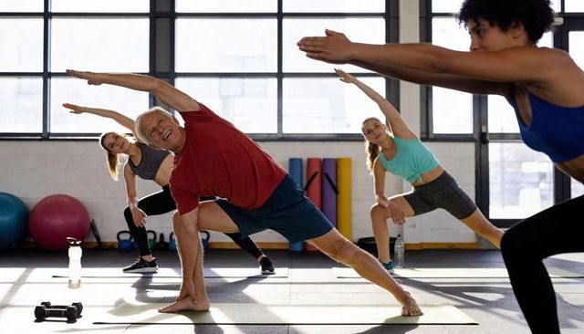 Senior man stretching in group fitness class with mixed-age participants in sunlit gym