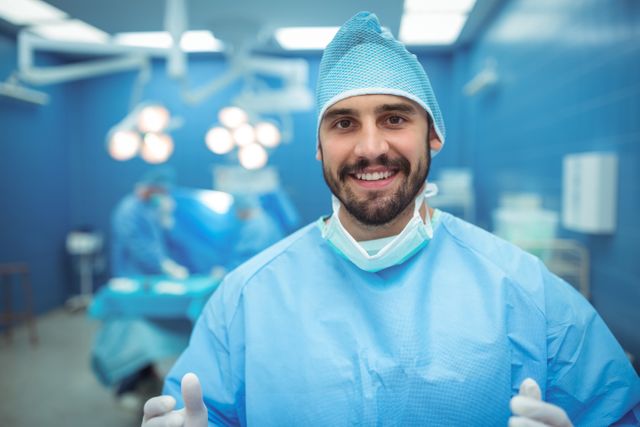Male surgeon smiling confidently in an operating room, wearing surgical scrubs and gloves. Ideal for healthcare, medical, and hospital-related content, showcasing professionalism and positive attitude in medical settings.