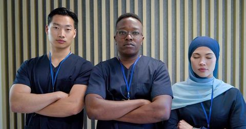 Diverse medical team standing with arms crossed in clinic wearing navy scrubs and hijab