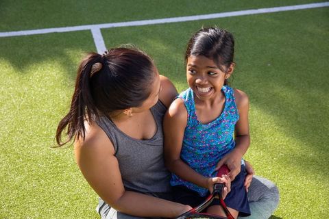 Mother and Daughter Smiling on Tennis Court Holding Racket