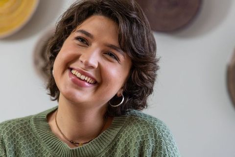 Smiling woman tilting head wearing green knit sweater, hoop earrings and beaded necklace