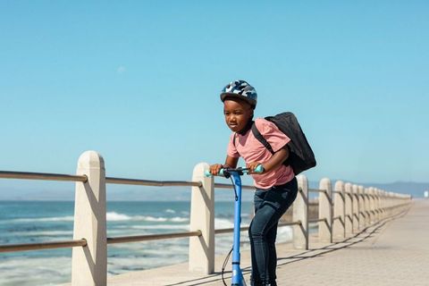 Child enjoying scooter ride along seaside promenade on sunny day