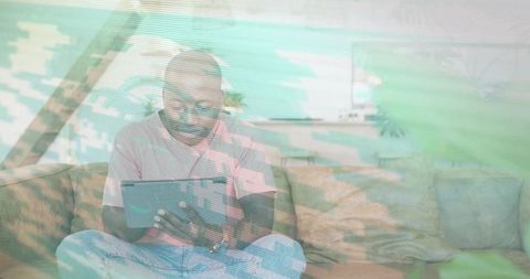 Man using tablet on sofa with green glitch overlay for remote work and streaming