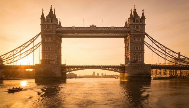 Tower bridge glowing at golden hour over river thames with rowing boat and reflections