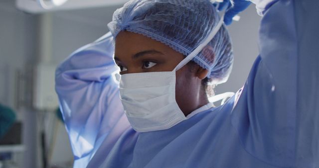 Image of african american female surgeon tying face mask in operating theatre. Hospital, medical and healthcare services.