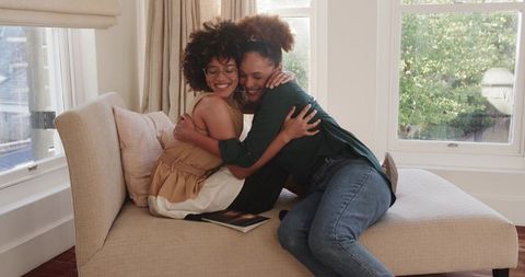 Sunlit Hug on Beige Chaise Between Two Women Sharing Warmth and Joy