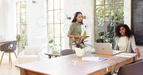Two women collaborating in bright modern workspace, working on laptop and documents