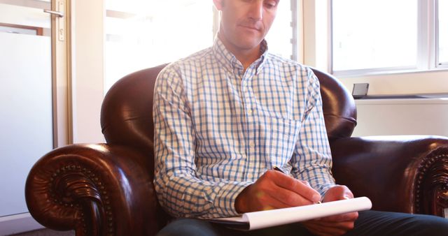 Man Writing Notes While Sitting on Leather Armchair in Sunlit Room - Download Free Stock Images Pikwizard.com