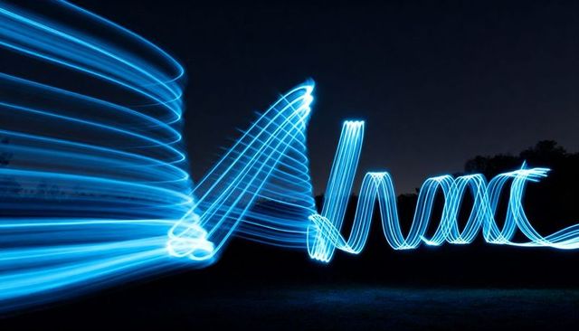 Electric-blue light trails swirling and spiraling above grassy field at night, neon motion