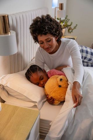 Loving Mother Tucking Daughter into Bed for Peaceful Sleep