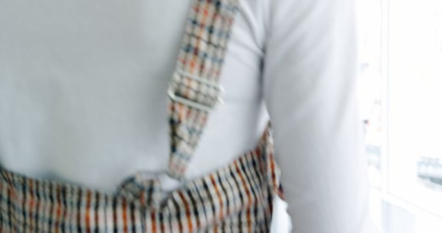 This stock photo captures a close-up of an individual wearing plaid strap clothing, pictured indoors. The focus is on the textured straps and the buckle detail, emphasizing casual wear and fashion. Use this image in articles or blogs about fashion trends, clothing design, textiles, or garments.
