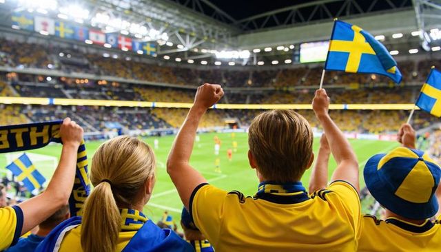Swedish fans cheering and waving flags in packed football stadium