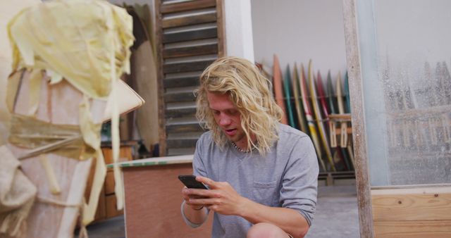 Young Man with Long Hair Using Smartphone in Surfboard Workshop - Download Free Stock Images Pikwizard.com