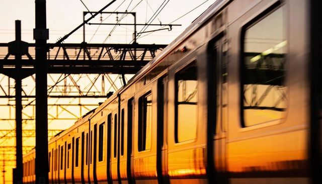 Passenger train reflecting golden sunset passing through urban rail network with catenary wires