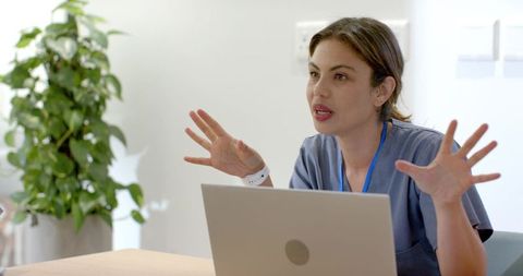 Female healthcare professional in blue scrubs gesturing during telehealth consultation