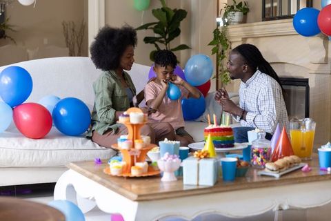 African american family celebrating birthday at home with rainbow cake, balloons, gifts