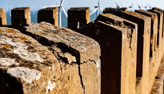 Weathered coastal parapet with cracked concrete posts and offshore wind turbines