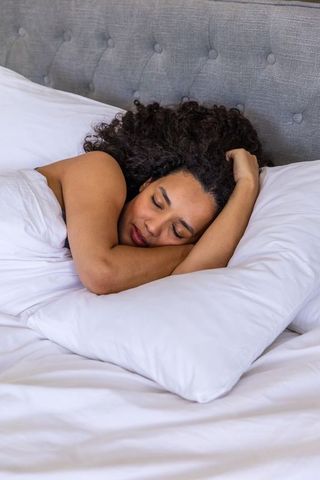Sleeping african american woman resting on white pillow on bed with gray tufted headboard