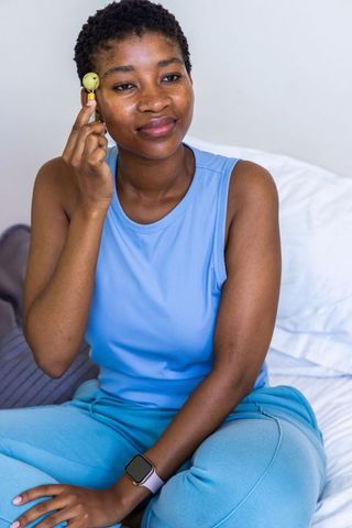Woman pressing facial roller on cheek wearing blue athleisure and smartwatch