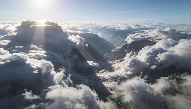 Sunlit alpine valley with towering clouds and crepuscular rays over winding river